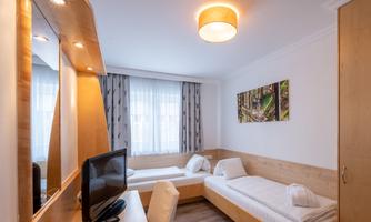 A modern room with two single beds and a desk. The walls are light, and there is a large window with curtains.