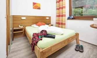 A simple bedroom with a comfortable bed and colorful curtains. There is a small table and a window that looks out to nature.