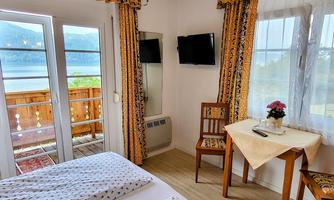 A cozy room with a view of a lake. There is a table, a chair, and a double bed with fresh linens.