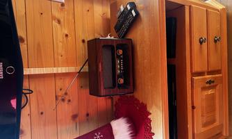 A wooden shelf with an old radio, a remote control, and a Santa hat. The wall is made of light wood, creating a cozy atmosphere.