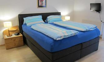 A cozy bedroom with a large double bed and light blue bedspreads. Two bedside tables with lamps and a television on the wall complete the room.