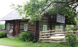 A charming wooden house with a balcony and green surroundings. The garden is adorned with a fence and many plants.
