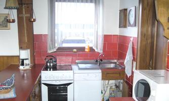 A small kitchen with red tiles and wooden details. There is a stove, a sink, and a refrigerator.
