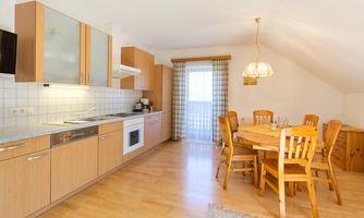 A bright kitchen with wooden cabinets and a wooden dining table.  
There are windows that let in a lot of light.