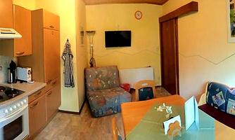 A cozy kitchen with a dining area and a sitting corner. The walls are painted in warm colors, and there is a television and some decorations.