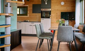 A modern kitchen and living unit with wooden paneling. The space has a bright, inviting character with a table and chairs.