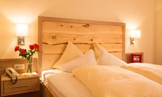 A cozy bedroom with a wooden bed and white pillows. Next to the bed are roses in a vase and a bedside lamp.