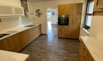 A modern kitchen with wooden cabinets and bright countertops. The space is well-lit and offers plenty of storage.