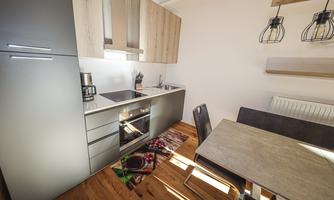 A modern kitchen with wooden and gray cabinets. There is a dining table and ample space for cooking.