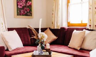 A cozy living room with a red sofa and decorative cushions. On the table is an arrangement of flowers and candles.