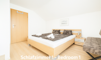 A modern bedroom with a large double bed and bright walls. There is a bedside table and a cozy seating area.