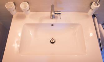 A modern sink with a shiny faucet. On it are two cups and a towel rack.