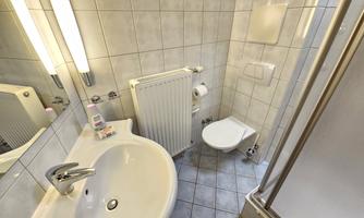 A modern bathroom with a sink, a toilet, and a shower. The walls are tiled and there is a radiator.