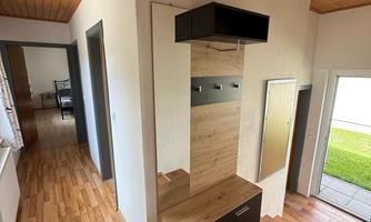 A modern entrance area with wooden flooring and a bright ambiance. On the left side, there is a practical cabinet with a shelf.
