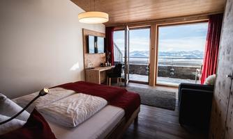 A modern room with wooden decor and a large window that offers a view of the mountains. The furnishings are cozy and inviting.