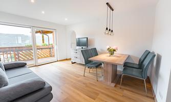 A modern living environment with a cozy sofa and a dining area. The room is bright and inviting, with a large window that lets in natural light.