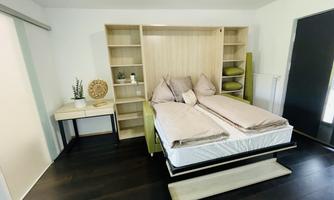 A modern bedroom with a bed and a wooden shelving system. The decor is minimalist and in neutral tones.