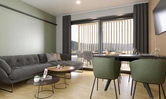 A modern living room with a gray sofa and a small table. Large windows provide a view of the outdoor landscape.