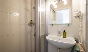 A modern bathroom with a shower, a small sink, and a mirror. The walls are brightly tiled, and there are some personal care products on the shelf.