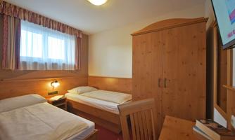 A simple room with two beds and a desk. There is a wardrobe and a television on the wall.
