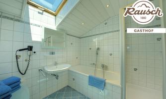 A bright bathroom with a bathtub and a shower. The walls are tiled and there are fresh towels in blue color.