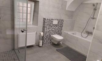 A modern bathroom with a bathtub and a shower. The walls are decorated with gray tiles and a decorative mosaic wall.