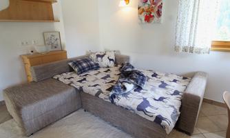 A cozy room with a sofa bed and a wool blanket. The room has bright walls, a window with curtains, and decorative pictures on the wall.