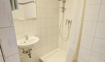 A small bathroom with a shower, sink, and toilet. The walls are tiled, and the furnishings appear modern and clean.