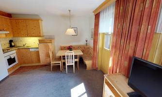 A cozy holiday apartment with a kitchenette, a dining table, and chairs. Large windows provide plenty of daylight and a welcoming atmosphere.