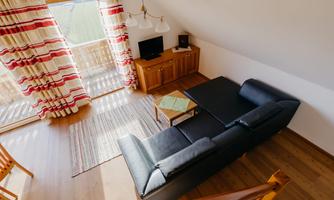 A cozy living room with a black sofa and a wooden table.  
Large windows with striped curtains provide plenty of light.