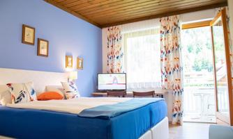 A bright and cozy bedroom with a comfortable bed and colorful curtains. The room features a television and a balcony overlooking the outdoors.