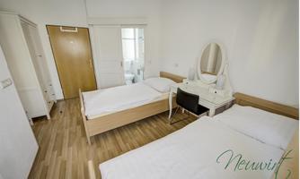 A simple room with two single beds and a large mirror. The room has light walls and a modern, minimalist style.