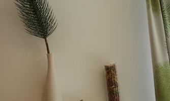 A simple wall shelf with a white vase containing a green branch. Next to it is a glass with decorative materials and a small wooden house.
