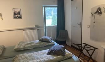 A simple room with two single beds and a window overlooking nature. There is a chair and a small table next to the beds.