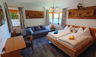 A cozy room with a double bed and a sofa bed. The wooden interior and the windows create a warm atmosphere.