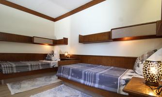 A cozy bedroom with two single beds and wooden shelves. There is warm lighting and a carpet on the floor.