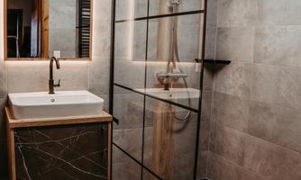 A modern bathroom with a walk-in shower and an elegant sink. The walls are kept in shades of gray and the light is soft and inviting.