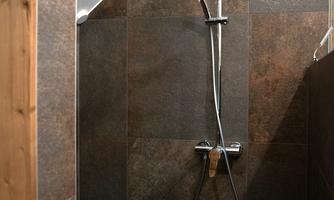 A modern shower with a rain showerhead and a hand shower. The walls are clad with dark tiles.