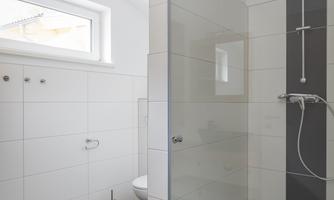 A modern bathroom with a walk-in shower and clear tiles. Plenty of light through the window and a simple, elegant decor.