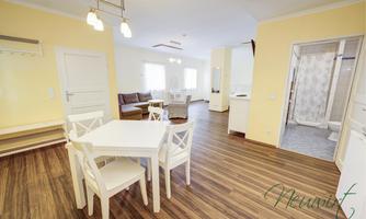 A bright, modern room with a dining area and an open kitchen. The space features a warm wooden floor and an inviting atmosphere.