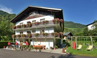 A charming house with blooming balcony plants in a green environment. In the foreground, there are garden furniture and a swing.
