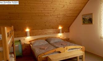 A cozy bedroom with a wooden ceiling and two beds. Next to a bunk bed, there is a small desk and a window with curtains.