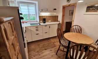 A cozy kitchen with a round table and two wooden chairs. The walls are bright and the furniture is modern and functional.
