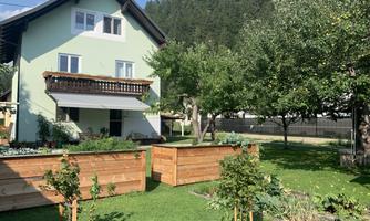 A beautiful house with a bright paint and a garden full of plants. In the background, trees and green meadows can be seen.