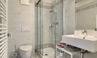 A modern bathroom with a shower, sink, and toilet. The walls are bright tiled and the room feels spacious and clean.