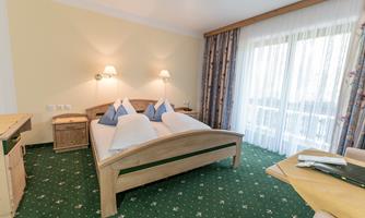 A cozy bedroom with two beds and a balcony. The room has a green carpet and light furniture.