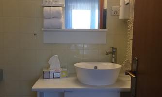 A simple bathroom with a modern sink and a large mirror. Towels and a box of tissues are visible.