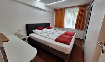 A cozy room with a double bed, red pillows, and light decor. The window lets in plenty of daylight and creates a friendly atmosphere.