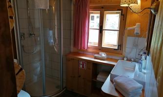 A modern bathroom in a wooden house with a shower, sink, and window. The decor is bright and inviting, with towels on the table.