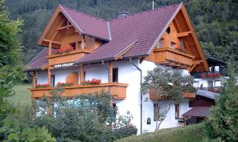 A charming wooden house with a red roof and beautiful flower boxes. Surrounded by green nature and gentle hills.